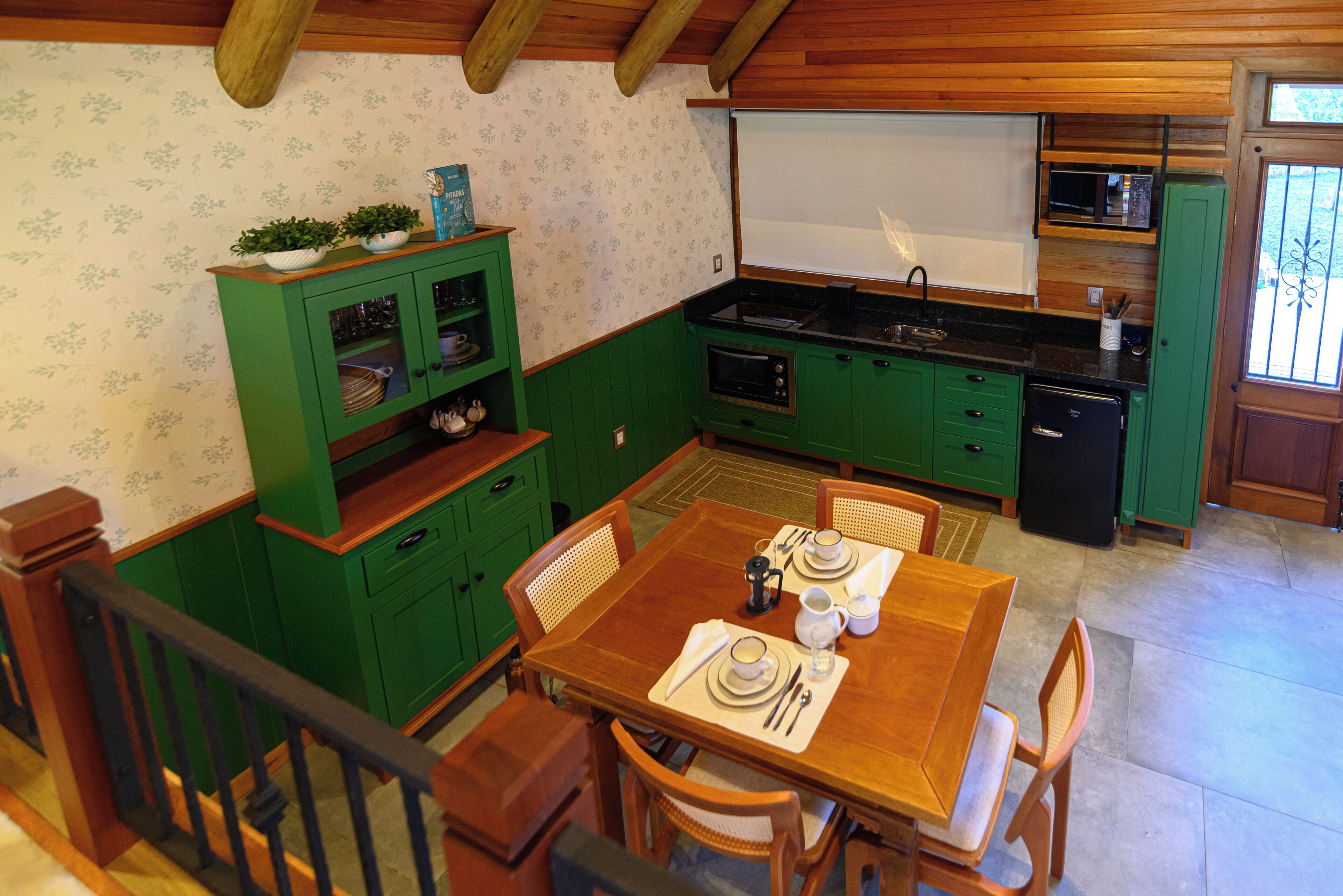 A kitchen with green cabinets, a wooden dining table set for two, and a small oven.