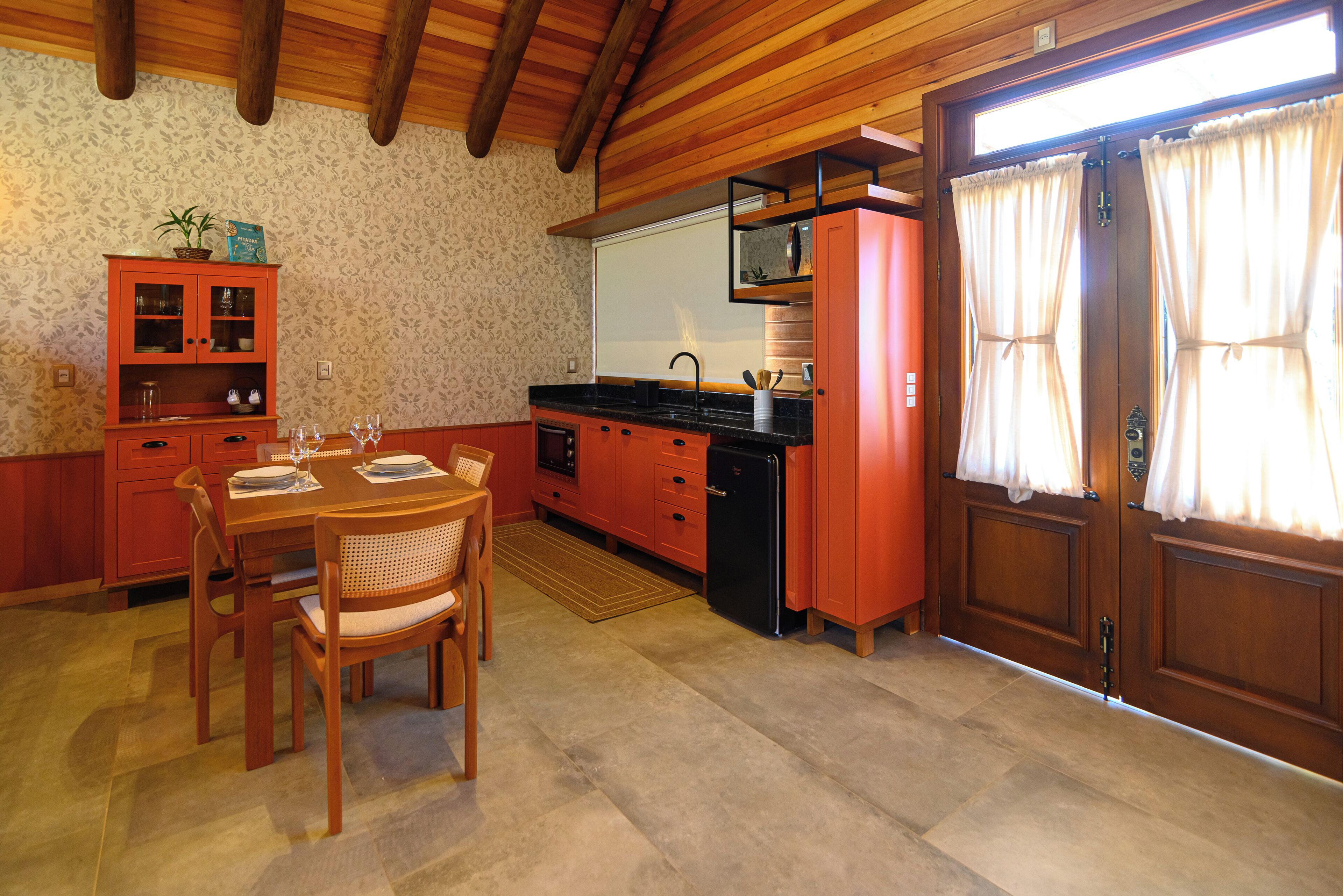 Une cuisine avec des meubles de rangement en bois, une table à manger avec des chaises et un four encastré.