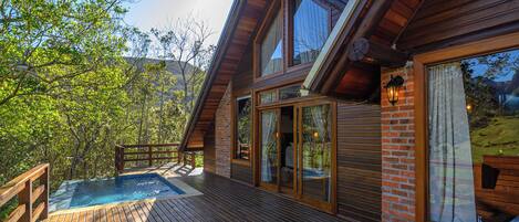 A wooden deck with a hot tub, large windows, and a brick wall.