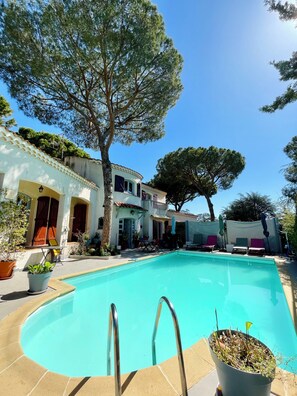 A swimming pool with a tiled deck, surrounded by potted plants and outdoor furniture. - Maison d'hôtes naturiste Villa PaulAna (Cap d'Agde)