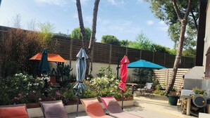 Eine Terrassenfläche mit Liegestühlen, Sonnenschirmen und Kübelpflanzen.