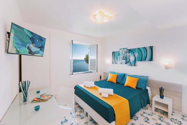 A modern bedroom with a large bed, a desk with a laptop, and artwork on the walls.