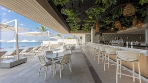 An outdoor seating area with tables and chairs, a bar, and a view of the sea. - BOSA HOTELS & RESIDENCES (Bucerias)