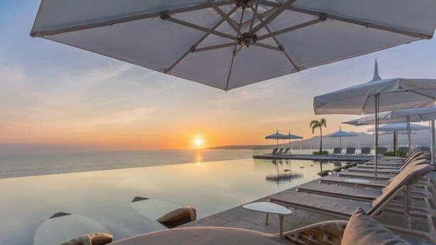 A serene infinity pool with lounge chairs and umbrellas, overlooking a sunset over the ocean. - BOSA HOTELS & RESIDENCES (Bucerias)