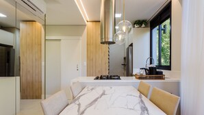 Une cuisine moderne avec une table à manger en marbre, des meubles de rangement en bois et des luminaires suspendus.
