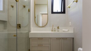 Une salle de bain moderne avec une douche à parois de verre, un grand miroir et un meuble-lavabo blanc doté de poignées dorées.