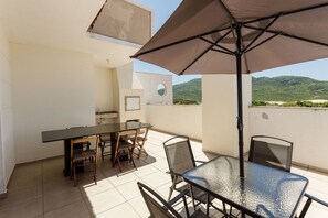 A patio with a table and chairs, an umbrella, and a view of a green landscape.