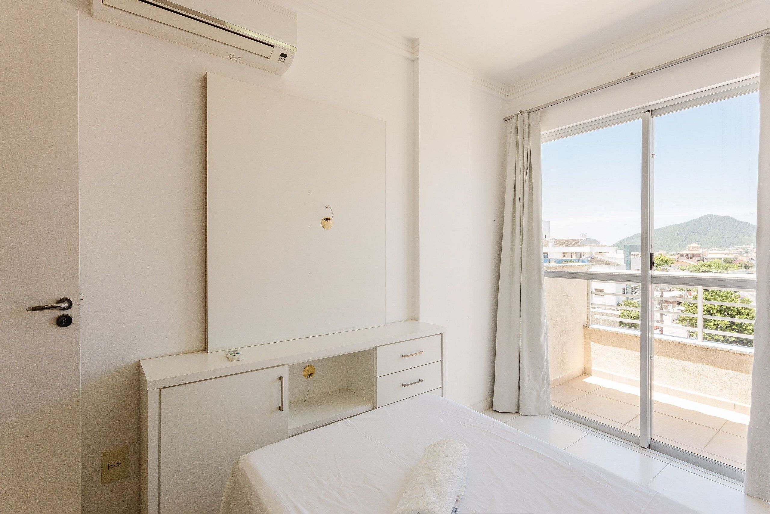 Una camera d'albergo con un letto, una scrivania, un armadio e un'ampia porta-vetrata scorrevole verso il balcone.
