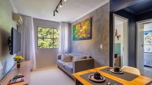 A modern room with a large window, a sofa, a dining table with chairs, and a TV. - Condominium in Floripa 300m From the Beach - CAS (Florianópolis)
