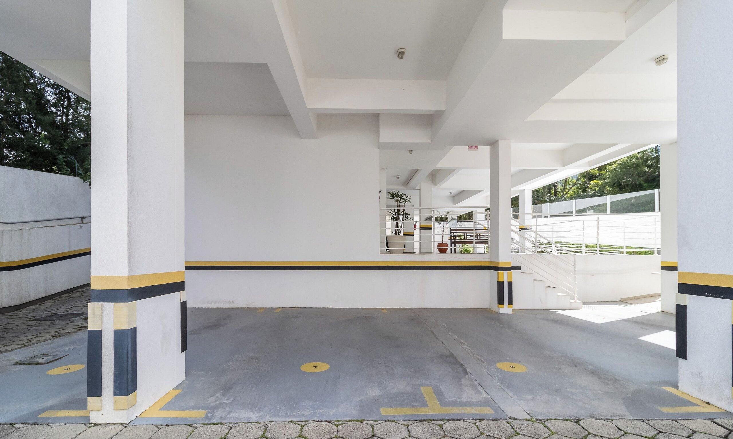 A covered parking area with white pillars, yellow and black stripes, and a ramp leading to a gated entrance.