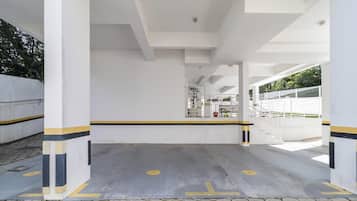 Un área de estacionamiento techada con pilares blancos, franjas amarillas y negras, y una rampa que conduce a una entrada con portones.