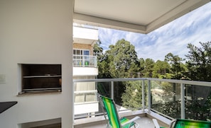 A balcony with two green-striped chairs, a small shelf, and a view of trees and buildings.