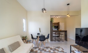 A modern living room with a sofa, a dining table with chairs, a TV, and a kitchen area in the background.