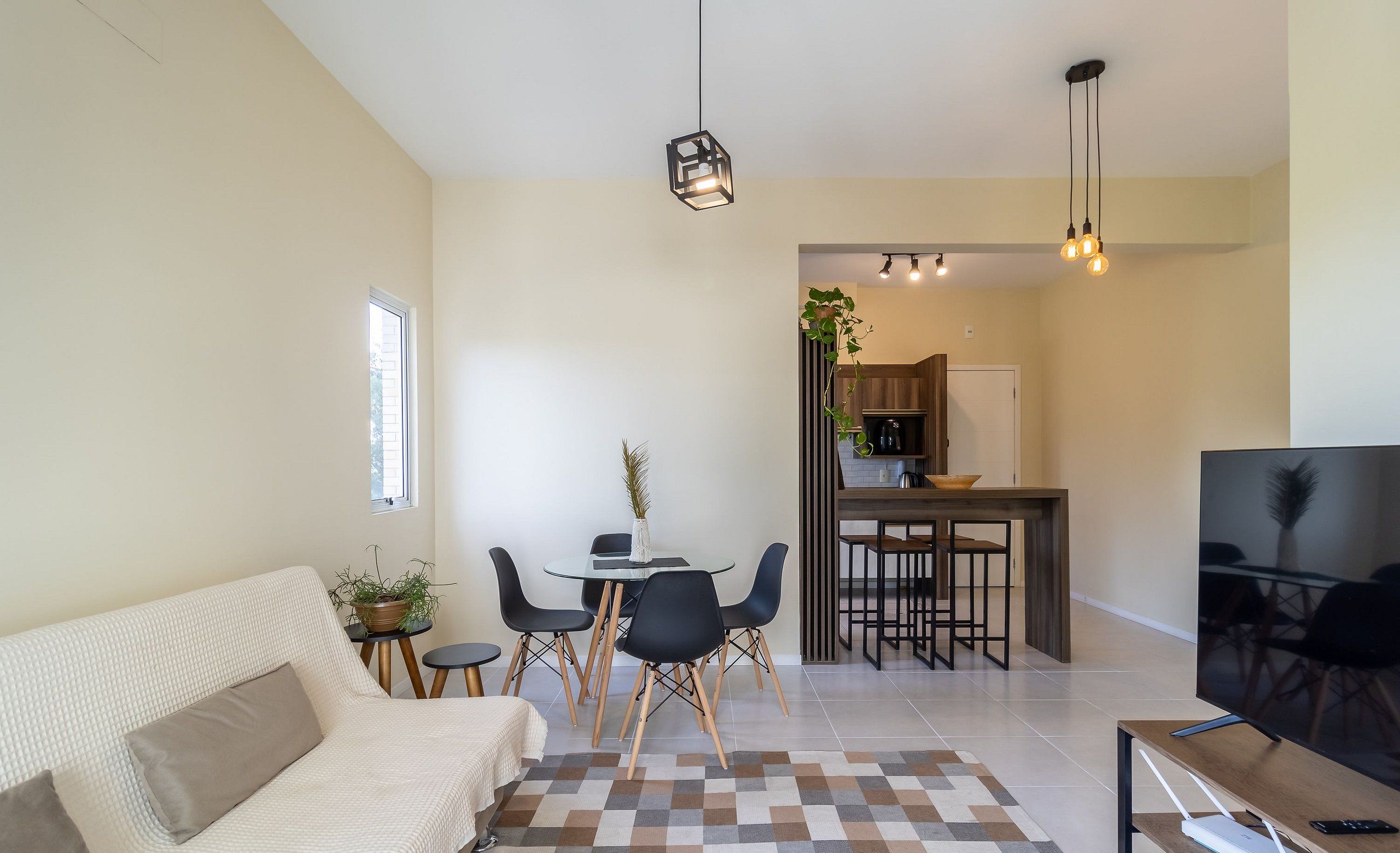En moderne stue med sofa, spisebord med stole, fjernsyn og et køkken i baggrunden.