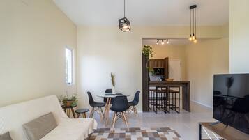Una sala de estar moderna con un sofá, una mesa de comedor con sillas, un televisor y una cocina al fondo.