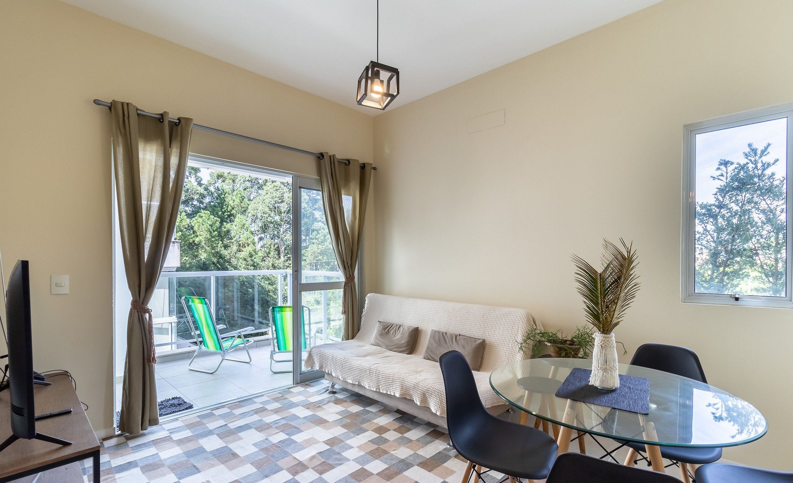 A modern living room with a glass table, black chairs, a beige sofa, and a view of the outdoors.