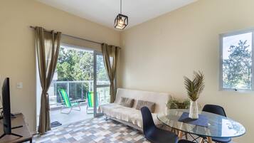 Un salón moderno con una mesa de vidrio, sillas negras, un sofá color crema y vistas al exterior.