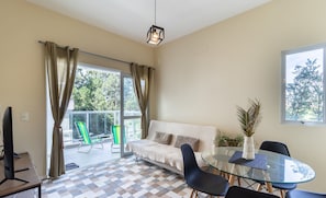 A modern living room with a glass table, black chairs, a beige sofa, and a view of the outdoors.
