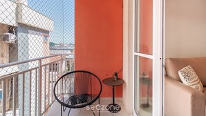 A balcony with a red wall, a black chair, a small table, and a beige sofa with a patterned pillow.