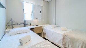 A hotel room with two beds, a desk, and a window.
