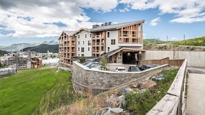A modern hotel with a stone retaining wall, multiple balconies, and a view of mountains.