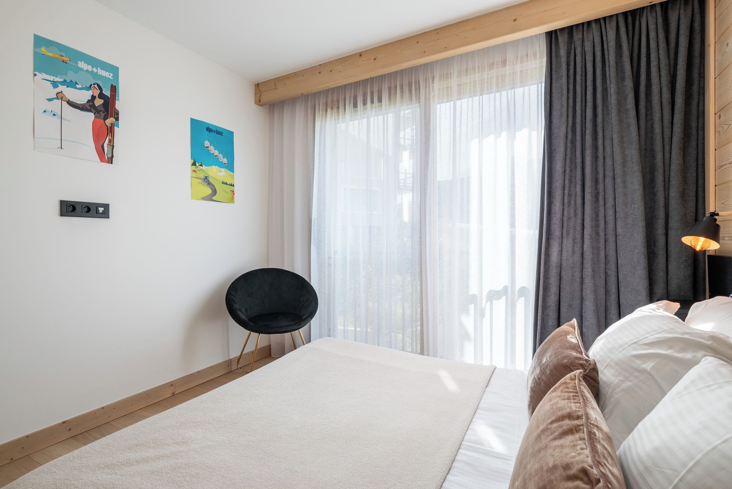 A bedroom with a bed, a chair, a window with curtains, and two wall posters.