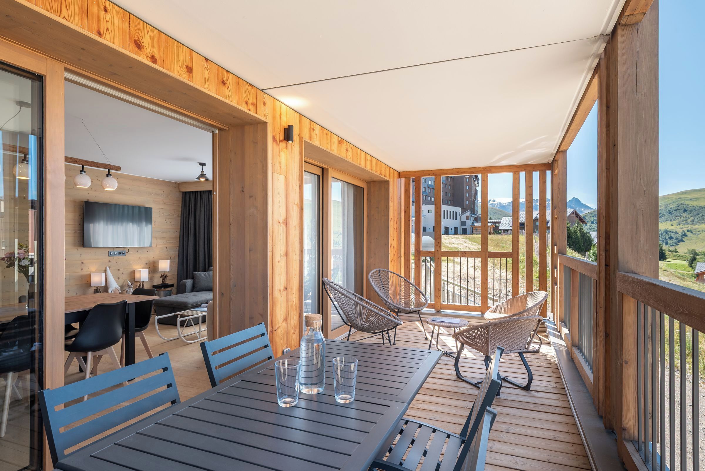 A wooden deck with a table and chairs, a sofa, and a TV in the background.
