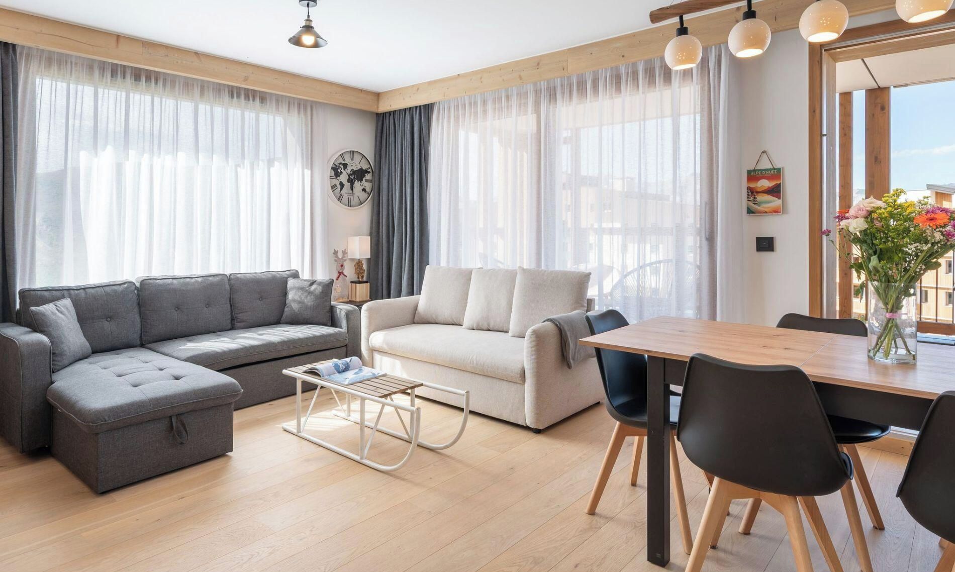 En moderne stue med en grå hjørnesofa, en hvid sofa, et træspisebord med sorte stole og lette gardiner.