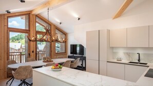 A modern kitchen with a marble countertop, wooden beams, and a large window overlooking a scenic landscape.