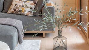 A modern living room with a grey sofa, a clear glass vase with branches, and wooden flooring.