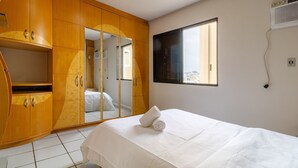 Una habitación de hotel con una cama, un armario, un ventanal y un espejo.