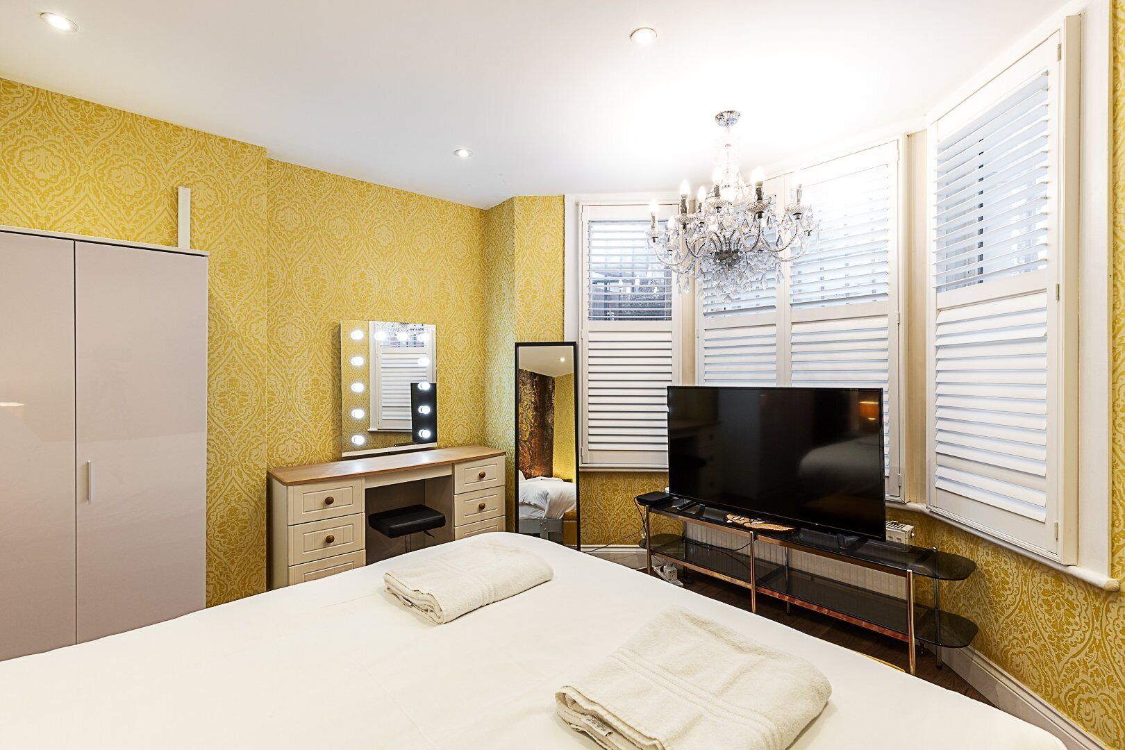 Een hotelkamer met een bed, een kaptafel met spiegel en verlichting, een televisie en een kroonluchter.