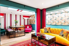Un salon moderne avec un canapé jaune, un divan rouge et un coin repas dont les murs sont recouverts d’un papier peint à rayures.