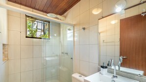 A modern bathroom with a glass shower enclosure, a toilet, a sink with a mirror, and a wooden ceiling.