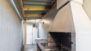 A narrow outdoor kitchen area with a built-in grill, a sink, and a wooden beam ceiling.