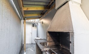 A narrow outdoor kitchen area with a built-in grill, a sink, and a wooden beam ceiling. - Cozy Apartment Just 2 min From the Sea! - Vig0011 (Florianópolis)