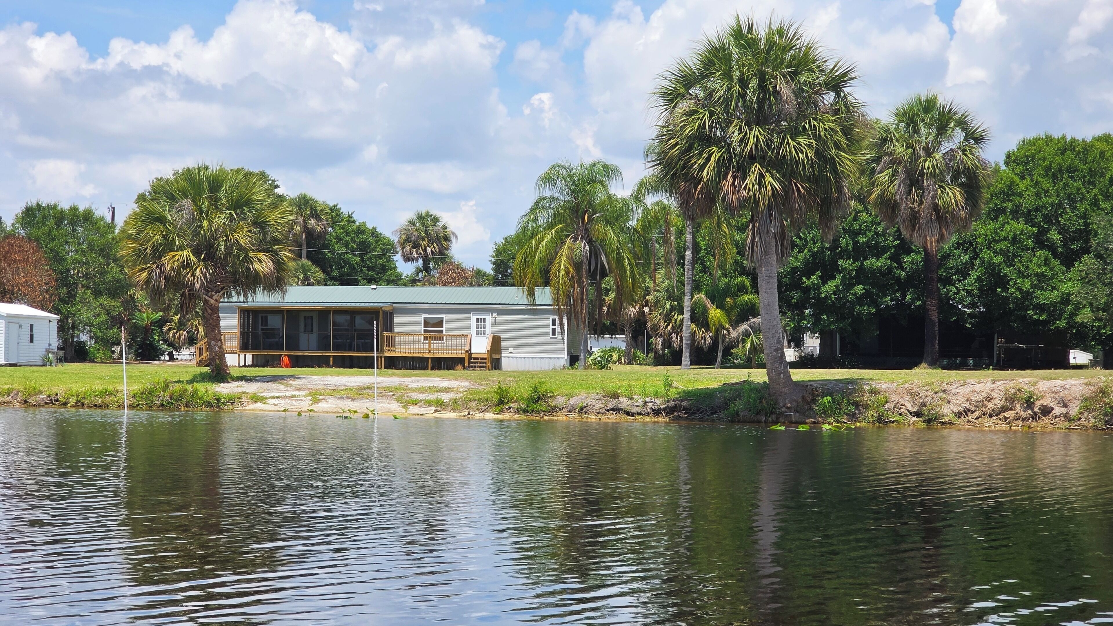 Propiedad frente al lago con una construcción de un solo nivel, un muelle y palmeras alrededor.