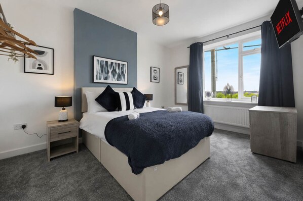 A modern bedroom with a bed, bedside table, lamp, artwork, and a view of the outdoors.