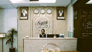 Un mostrador de recepción con relojes que muestran la hora de Londres, Kuwait y Nueva York, una recepcionista y el logotipo de Safari Hotel Apartments.