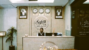 Vastaanottotiski, jossa on kelloja, joista näkyy Lontoon, Kuwaitin ja New Yorkin aika, vastaanottovirkailija sekä Safari Hotel Apartments -hotelliketjun logo.