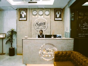 Ein Empfangsschalter mit Uhren, die die Zeiten von London, Kuwait und New York anzeigen, eine Rezeptionistin und das Logo der Safari Hotel Apartments.
