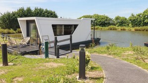A modern, white floating structure with a glass enclosure, a small deck, and a pathway leading to it. - Riverside Exclusive Retreat (Newquay)