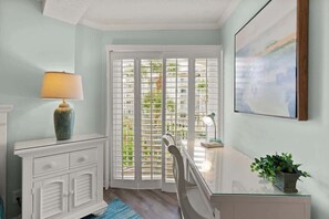 A room with a white cabinet, a lamp, a desk with a lamp, a chair, and a potted plant.
