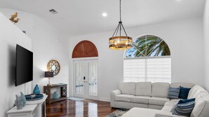 A living room with a flat-screen TV, a sofa, a coffee table, and a chandelier.