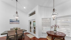 A dining area with a wooden table and chairs, two hanging light fixtures, and a painting on the wall.