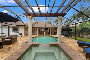 Une piscine extérieure couverte, agrémentée d’une pergola, de chaises longues et d’une terrasse dallée de pierres.