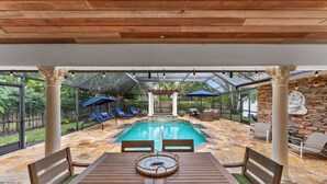 An outdoor pool area with a wooden table and chairs, surrounded by stone walls and covered by a glass roof.