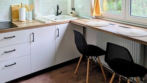 Una cocina moderna con armarios blancos, encimera de madera, una silla negra y una ventana con vistas a zonas verdes.