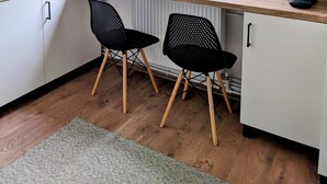 Una cocina moderna con armarios blancos, encimera de madera, dos sillas negras, una ventana con cortinas y una planta colgante.