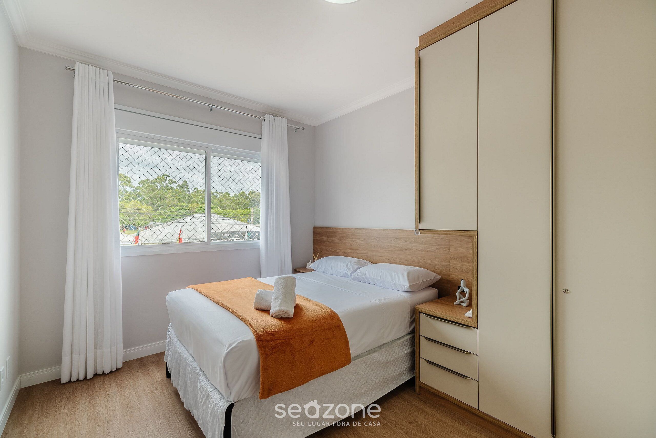 A bedroom with a bed, a nightstand, a wardrobe, and a window with curtains.